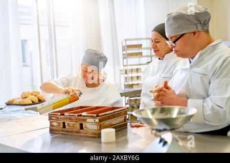 Koch und Studenten mit Down-Syndrom, die Brot in der Küche backen Stockfoto