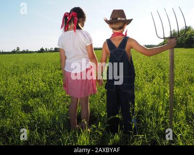 Kleines Mädchen und ein Junge halten einen Rechen in der Grünes Feld Stockfoto