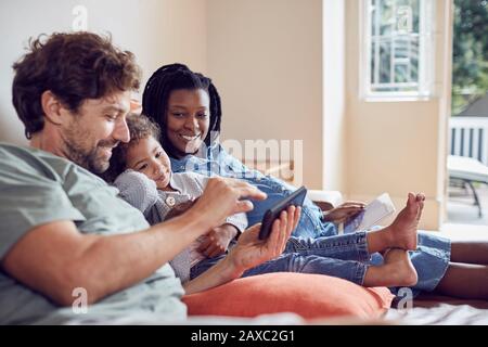 Schwangere junge Familie mit Smartphone und digitalem Tablet auf dem Sofa Stockfoto