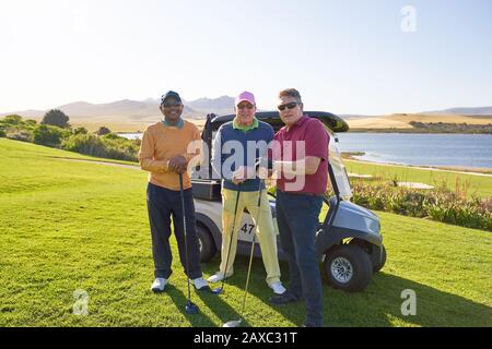 Portrait selbstbewusste männliche Freunde, die auf einem sonnigen Golfplatz Golf spielen Stockfoto