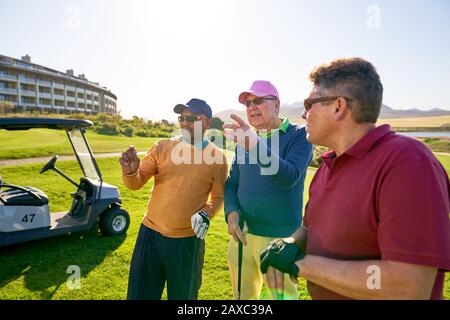 Männliche Golfspielerfreunde, die auf einem sonnigen Golfplatz sprechen Stockfoto