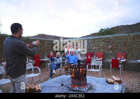 Senior befreundet mit Wein, der für Fotos in der Feuerstelle auf der Terrasse posiert Stockfoto