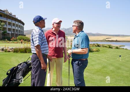 Glückliche männliche Golfspielerfreunde, die auf einem sonnigen Golfplatz sprechen Stockfoto