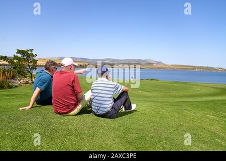 Männliche Golfer entspannen sich beim Blick auf den See vom sonnigen Golfplatz Stockfoto