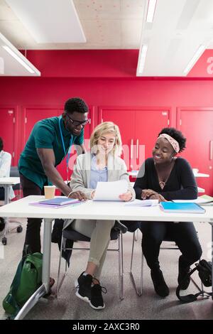 Community College-Kursleiter hilft Studenten am Schreibtisch im Klassenzimmer Stockfoto