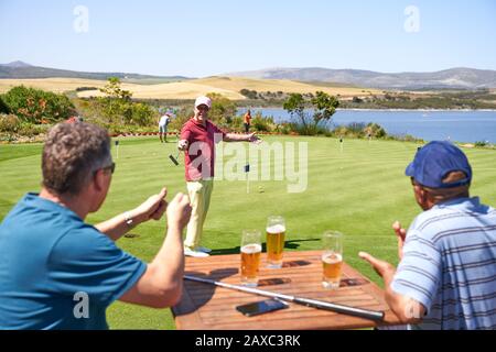 Glückliche männliche Golfer, die Bier trinken und auf dem Golfplatz spielen Stockfoto