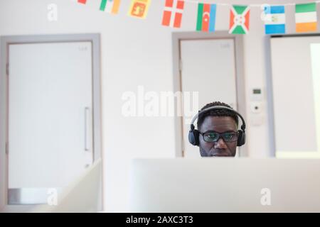 Student der männlichen Community mit Kopfhörern am Computer im Klassenzimmer Stockfoto