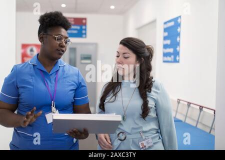 Hausärztin und Krankenschwester machen Umläufe und diskutieren die Krankenakte im Krankenhauskorridor Stockfoto