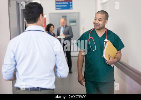Lächelnder männlicher Chirurg grüßt vorbeifahrenden Arzt auf Krankenhausflur Stockfoto
