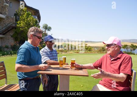 Glückliche reife männliche Golfer trinken Bier im sonnigen Golfplatzenklubhaus Stockfoto