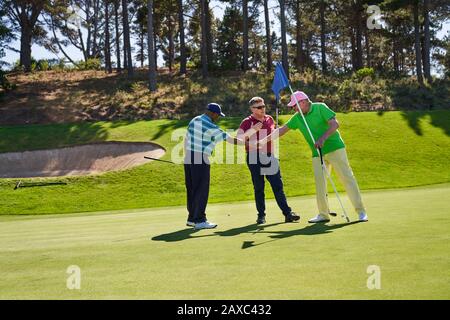 Männliche Golfer schütteln die Hände auf dem sonnigen Golfplatz und setzen Grün Stockfoto