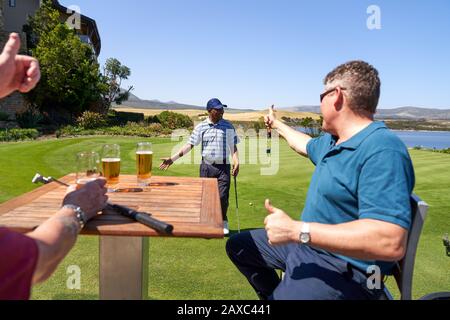 Männliche Golfer, die Bier trinken, jubelten Freund über die Praxis, Grün zu setzen Stockfoto