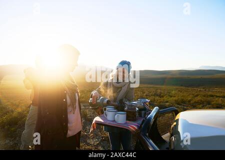 Glückliche ältere Frau auf Safari, die Tee für Freunde bei Sonnenaufgang gießt Stockfoto