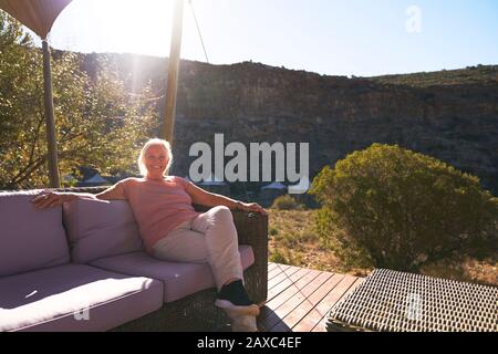 Sorgenfreie Seniorin, die sich auf dem sonnigen Balkon der Safari-Lodge entspannen kann Stockfoto