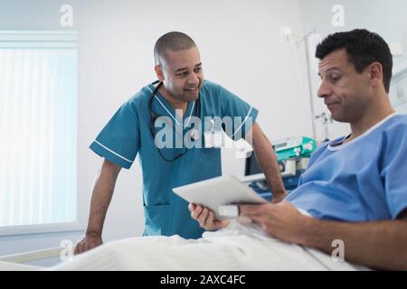 Pflegepersonal spricht mit dem Patienten über ein digitales Tablett im Krankenhausbett Stockfoto