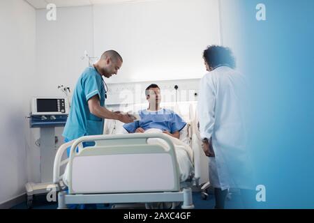 Ärzte mit digitaler Tablette runden das Gespräch mit dem Patienten im Krankenhauszimmer ab Stockfoto