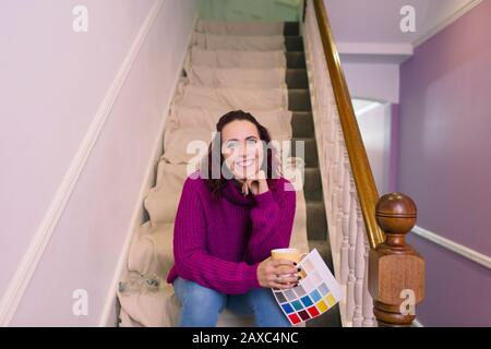 Portrait selbstbewusste Frau, die sich umschmückt und Farbmuster auf der Treppe hält Stockfoto