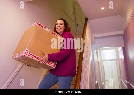 Portrait lächelnde Frau, die das Haus umzieht und Pappkarton auf einer Treppe trägt Stockfoto