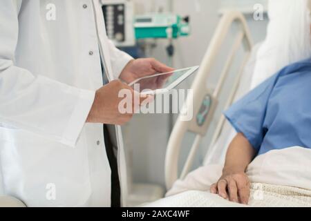 Arzt mit digitaler Tablette rundet ab und überprüft den Patienten im Krankenhausbett Stockfoto