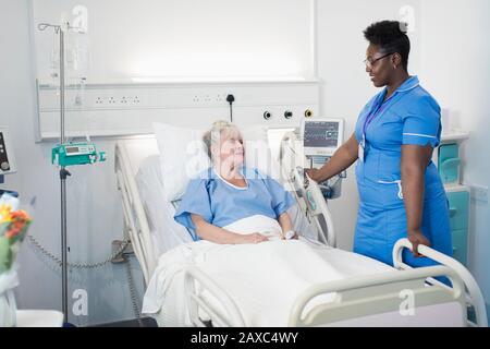 Weibliche Krankenschwester im Krankenhauszimmer, die mit einer älteren Patientin spricht Stockfoto