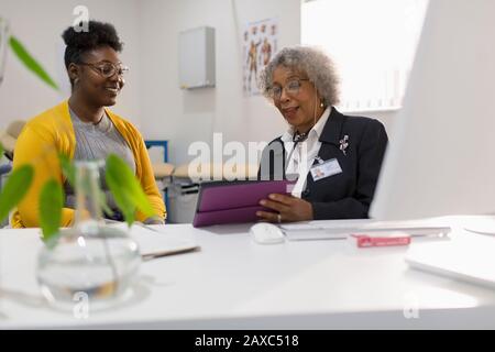 Weiblicher Arzt mit digitaler Tablette, das mit dem Patienten in der Arztpraxis zusammenkam Stockfoto