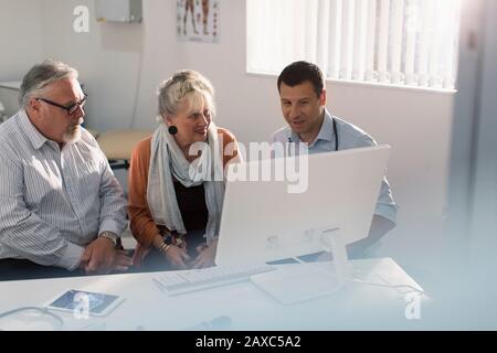 Arztbesprechung mit dem Senioren-Paar am Computer im Arztbüro Stockfoto