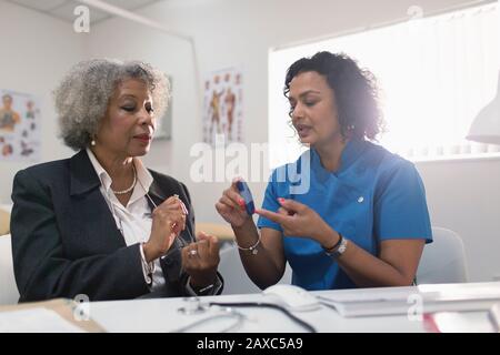 Hausärztin unterrichtet Diabetikerin, wie man Glukosimeter in der Arztpraxis verwendet Stockfoto