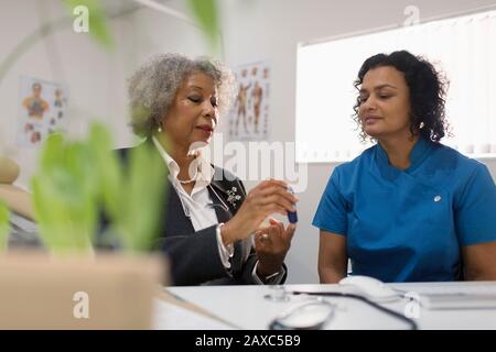 Hausärztin unterrichtet Diabetikerin, wie man Glukosimeter in der Arztpraxis verwendet Stockfoto