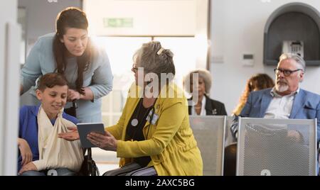 Weibliche Ärztin mit digitaler Tablette im Gespräch mit Mutter- und Jungpatienten in der Lobby der Klinik Stockfoto