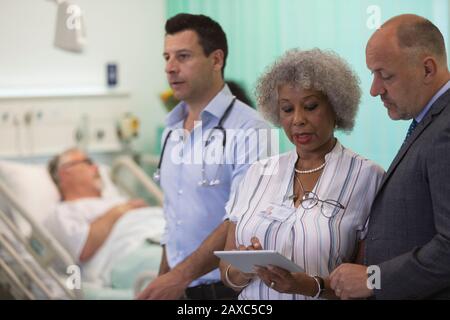 Ärzte mit digitaler Tablette runden ab und beraten im Krankenhauszimmer Stockfoto