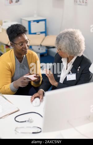 Weibliche Ärztin, die sich mit dem Patienten am Computer in der Arztpraxis zusammentat Stockfoto