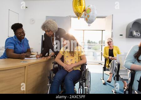 Girlpatient im Rollstuhl beim Einchecken an der Klinikrezeption Stockfoto