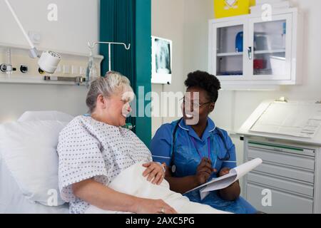 Weibliche Krankenschwester im Krankenhauszimmer mit einer älteren Patientin sprechen Stockfoto