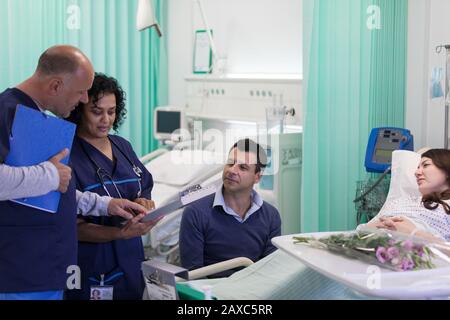 Ärzte mit medizinischen Diagrammen, die Runden ziehen und mit einem Paar in der Krankenstation sprechen Stockfoto