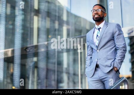 Junger, versierter unternehmer des afroamerikanischen CEO, stilvoller Anzug und Brille, die selbstbewusst im Bürogebäude des Arbeitsplatzes stehen Stockfoto