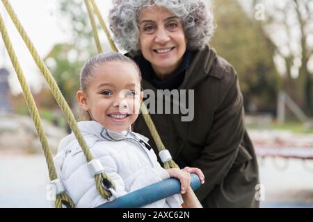 Portrait lächelnde Großmutter und Enkelin, die auf dem Spielplatz auf Schaukel spielen Stockfoto