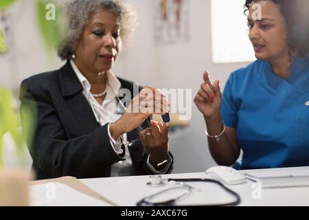 Hausärztin unterrichtet diabetische Oberpatientin über den Einsatz von Glukosimeter Stockfoto