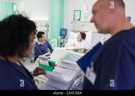 Ärzte mit medizinischen Diagrammen machen Umläufe mit Patienten, die im Krankenbett im Hintergrund ruhen Stockfoto