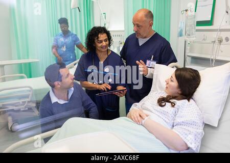 Ärzte mit digitalen Tabletts machen Runden und sprechen mit Paaren in der Krankenstation Stockfoto