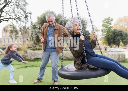 Verspielte Großeltern und Enkelin, die im Park auf dem Schaukel spielen Stockfoto