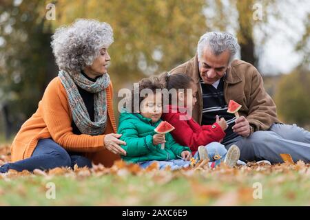 Großeltern und Enkel essen Wassermelone im Herbstpark Stockfoto