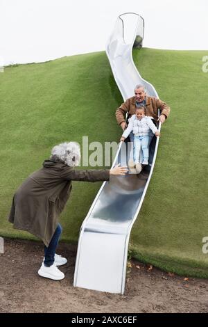 Großeltern mit Enkelin auf Spielplatzrutsche Stockfoto