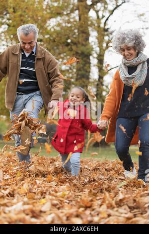Verspielte Großeltern und Enkelin treten Herbstlaub im Park Stockfoto