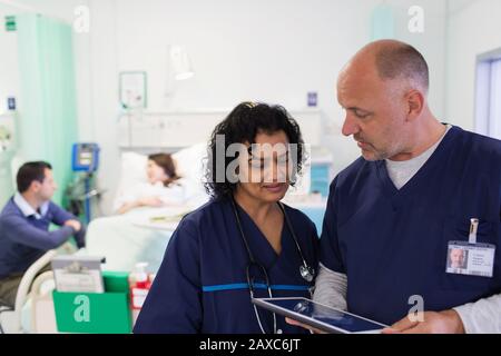 Ärzte mit digitaler Tablette runden ab und beraten im Krankenhauszimmer Stockfoto