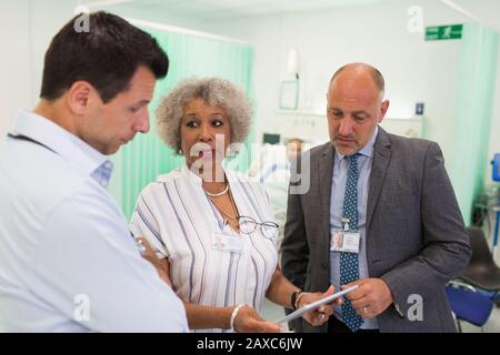 Ärzte mit digitaler Tablette runden ab und beraten im Krankenhauszimmer Stockfoto