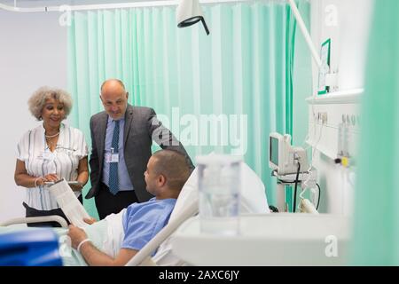 Ärzte machen Runden und sprechen mit der Zeitung "Patient liest" im Krankenhauszimmer Stockfoto