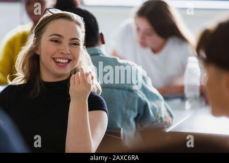 Fröhliche, lächelnde Schülerin der High School, die mit Klassenkameradin im Klassenzimmer spricht Stockfoto
