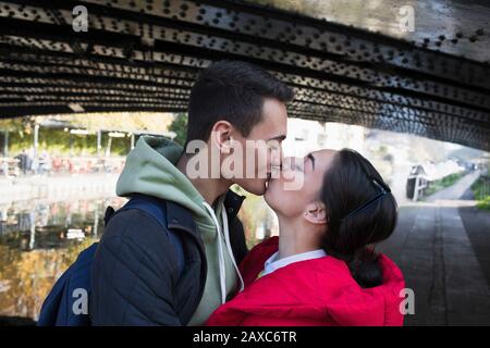 Liebevolles junges Paar, das unter Brücke küsst Stockfoto