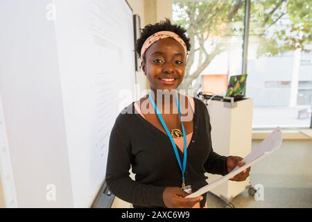 Portrait lächelnde, selbstbewusste Instruktorin mit Papierarbeit, die die Lektion auf der Projektionsleinwand im Klassenzimmer führt Stockfoto