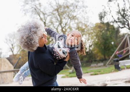 Portrait verspielte Großmutter hebt Enkelin auf dem Spielplatz Stockfoto